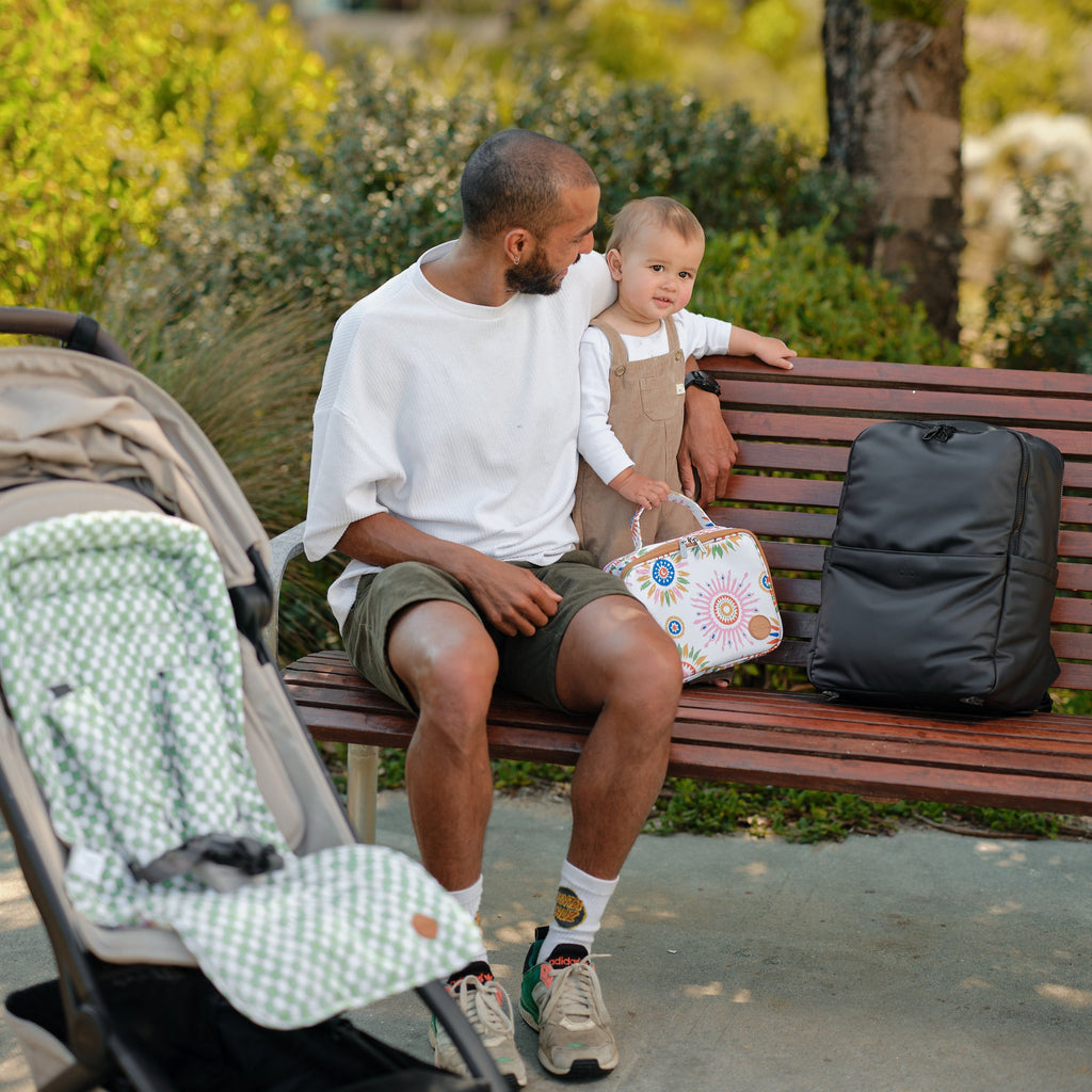 Man and child sitting on a park bench with a stroller nearby