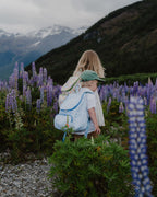 Two children with backpacks standing in a field of purple flowers with mountains in the background